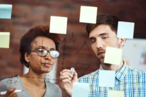 Descrição da imagem: Imagem mostra uma jovem aprendiz participando de reunião com colegas, representando habilidades comportamentais como comunicação e trabalho em equipe.